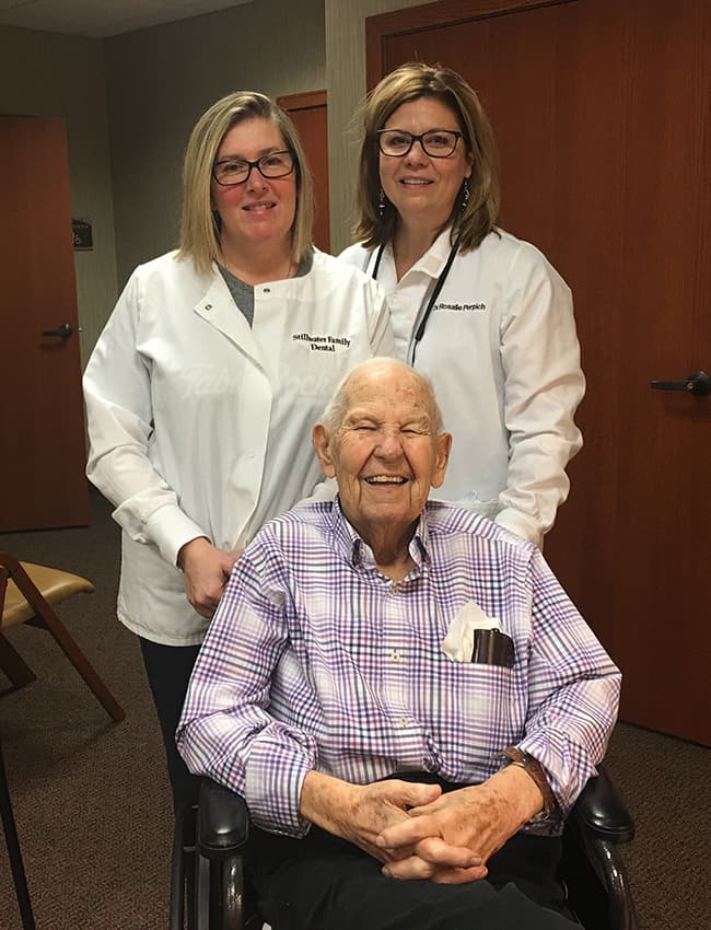The dentist and a team member smiling together with an older patient