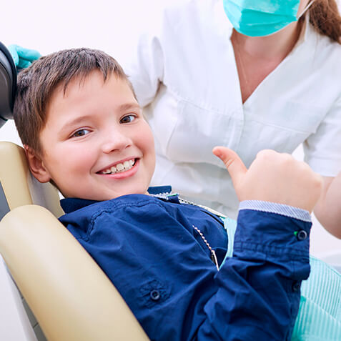 A young boy in a dental chair smiling 
